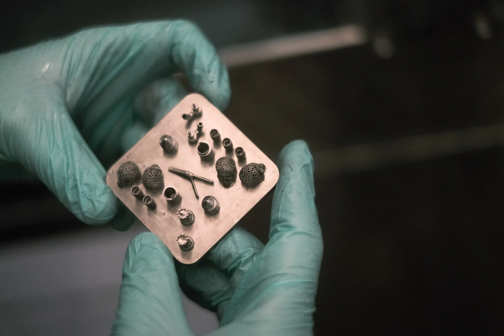 Mitarbeiter der 3D MicroPrint GmbH hält eine gedruckte Plattform mit mehreren 3D-gedruckten Bauteilen in der Hand